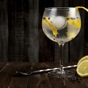 A close-up of a refreshing gin cocktail with lemon slices on a rustic wooden table, perfect for summer.