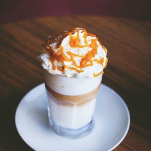 A delectable glass of caramel layered coffee topped with whipped cream on a wooden table.